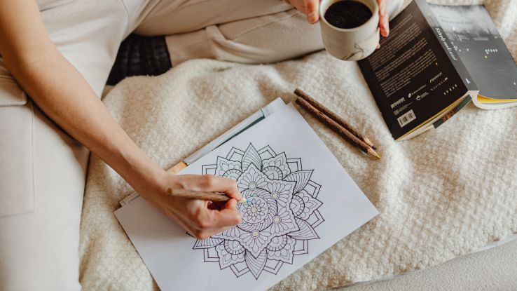 A woman enjoys a cozy moment with coloring, books, and coffee on a soft bed.