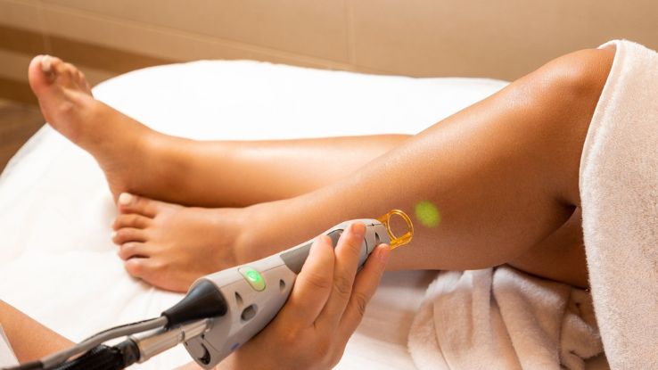 Close-up of a professional cosmetologist performing laser hair removal on a woman's leg in a spa.