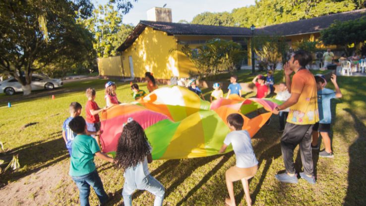 Group of children playing with a colorful parachute outside during a sunny day party.