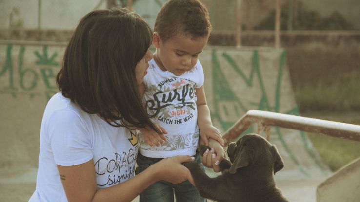 A loving moment between a mother, her child, and a playful puppy captured in an outdoor setting, evoking togetherness.