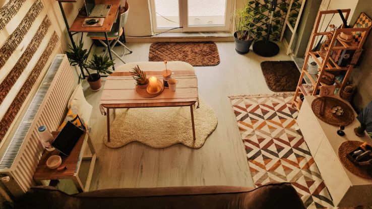 A cozy, warmly lit living room featuring a wooden desk, indoor plants, and decorative lights.