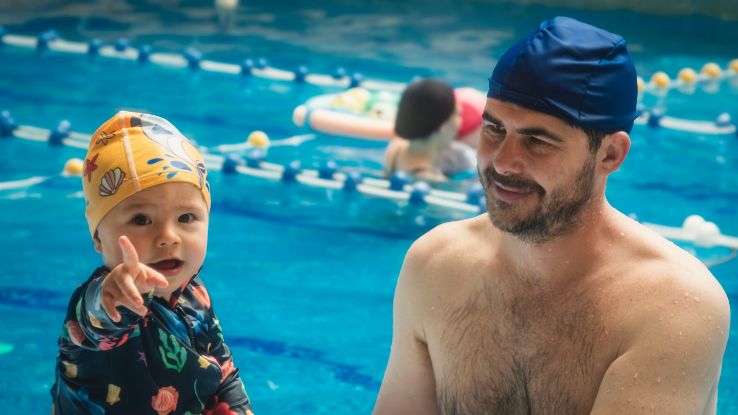Father and child bond during a swimming lesson at an indoor pool.
