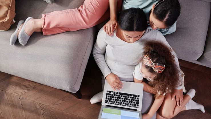 Mother and daughters enjoy quality time using a laptop on the couch.