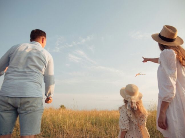 A family in a field flying a kite under a clear blue sky.